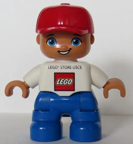 Duplo Figure Lego Ville, Child Boy, Blue Legs, White Top, Red Cap LEGO Logo and 'LEGO STORE UŠĆE' on Front
